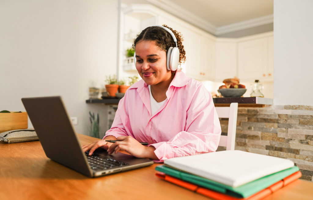 Girl attending Online Hindi Courses from home, studying with a laptop and headphones at a desk with notebooks.