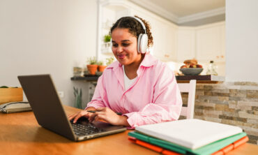 Girl attending Online Hindi Courses from home, studying with a laptop and headphones at a desk with notebooks.